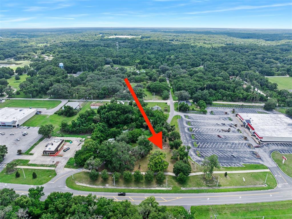 An aerial view shows a vacant, tree-covered lot situated between two commercial parking lots — 1101 N SUMMIT STREET, CRESCENT CITY, FL