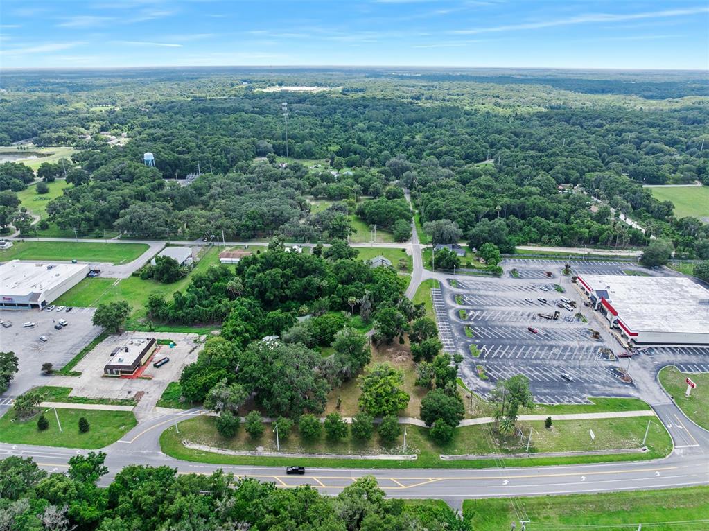 An aerial view shows a wooded lot situated between two commercial parking lots and roads — 1101 N SUMMIT STREET, CRESCENT CITY, FL