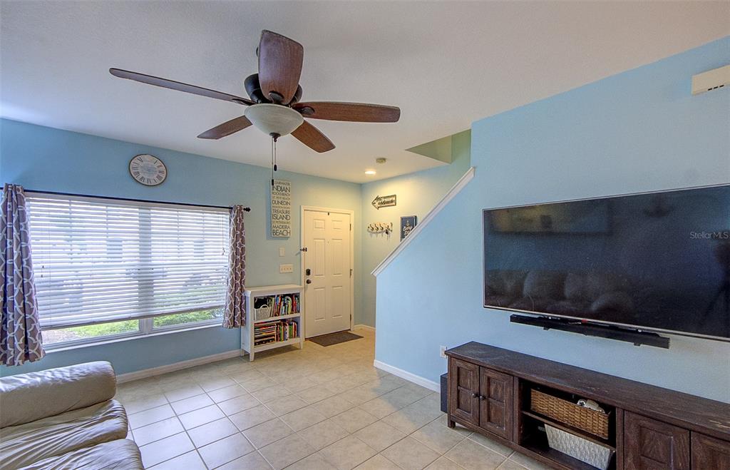 A living room with light blue walls, tile flooring, a ceiling fan, and a television — 4643 67TH AVENUE N, PINELLAS PARK, FL