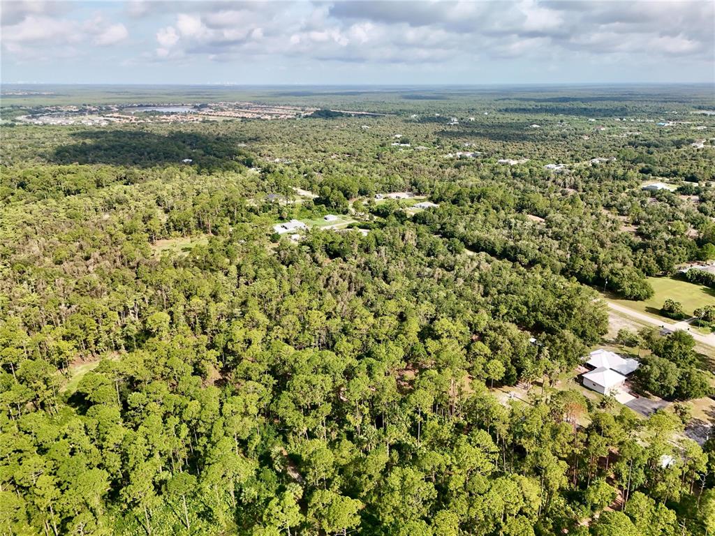 An aerial view shows a dense forest with scattered houses and a distant residential development — 260 35TH AVENUE NW, NAPLES, FL