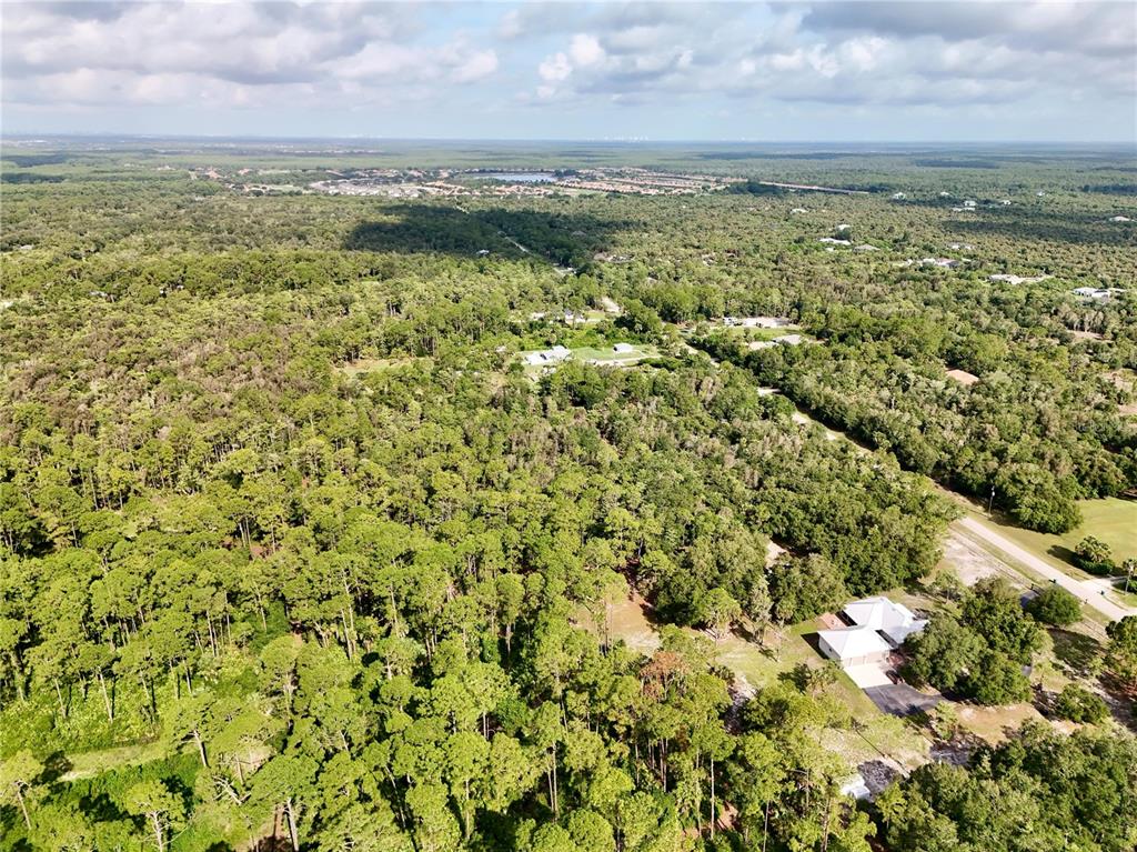 An aerial view shows a house surrounded by dense forest and scattered residential properties — 260 35TH AVENUE NW, NAPLES, FL