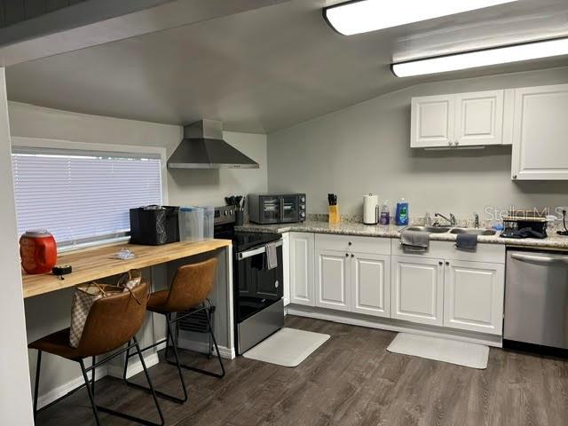 A kitchen features white cabinets, a black stove, a breakfast bar, and wood-look flooring — 325 S 2ND STREET UNIT 206, LEESBURG, FL
