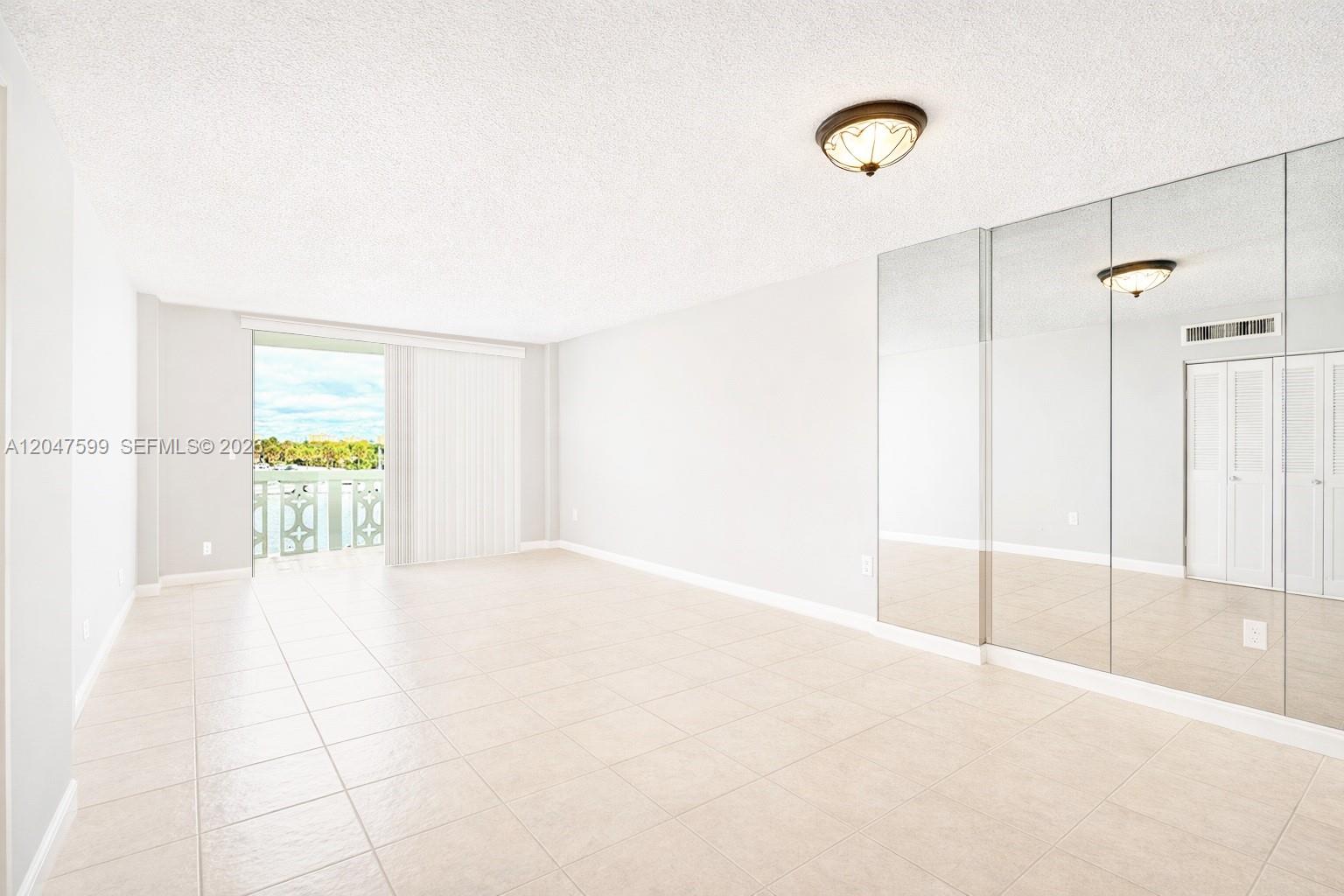 A bright room features light tile flooring, mirrored closet doors, and a sliding glass balcony door — 13155 Ixora Ct # 310, North Miami FL 33181, NORTH MIAMI, FL
