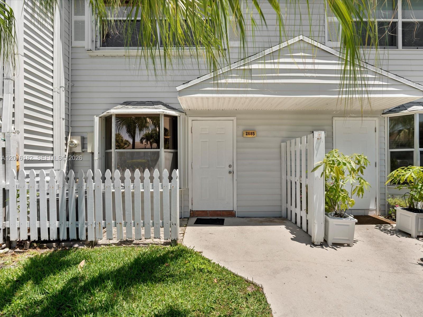 The exterior of a two-story townhouse features light gray siding, a white picket fence, and a front door — 2685 NE 15th St, Pompano Beach FL 33062, POMPANO BEACH, FL