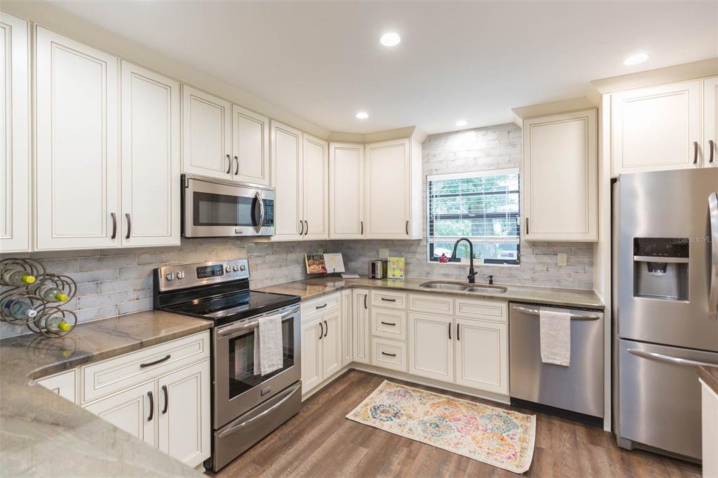 A kitchen with white cabinets, stainless steel appliances, a tile backsplash, and wood-look flooring — 702 W BAY STREET UNIT A, TAMPA, FL