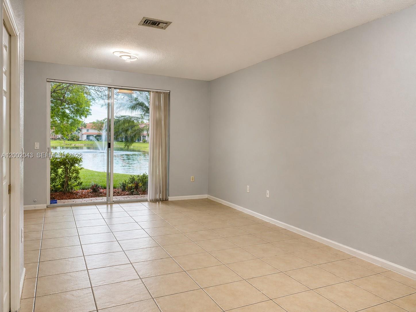 An empty room with light-colored tile flooring and a sliding glass door overlooking a pond — 2741 SW 83rd Ave # 104, Miramar FL 33025, MIRAMAR, FL