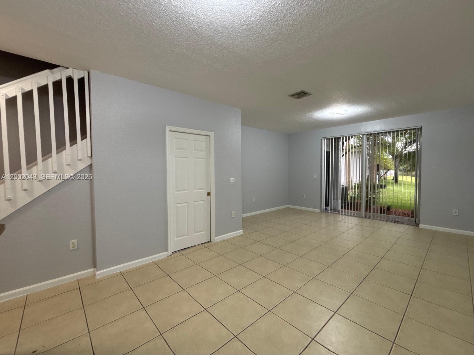 An empty living room features light-colored tile floors, a white staircase, and sliding glass doors — 2741 SW 83rd Ave # 104, Miramar FL 33025, MIRAMAR, FL
