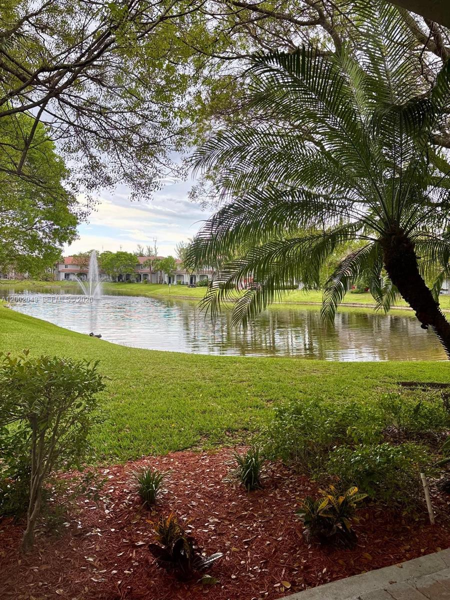 A view of a pond with a fountain, surrounded by grass, trees, and residential buildings — 2741 SW 83rd Ave # 104, Miramar FL 33025, MIRAMAR, FL