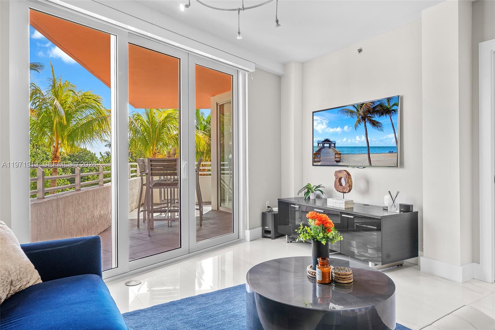 A modern living room features a blue sofa, circular coffee table, and sliding glass balcony doors — 226 Ocean Dr # 3C, Miami Beach FL 33139, MIAMI BEACH, FL