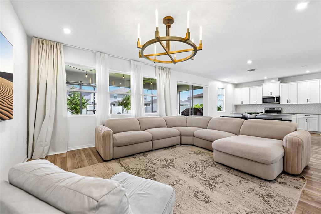 A living room with a large sectional sofa, chandelier, and open kitchen in the background — 2960 ANGELONIA THORN WAY, CLERMONT, FL