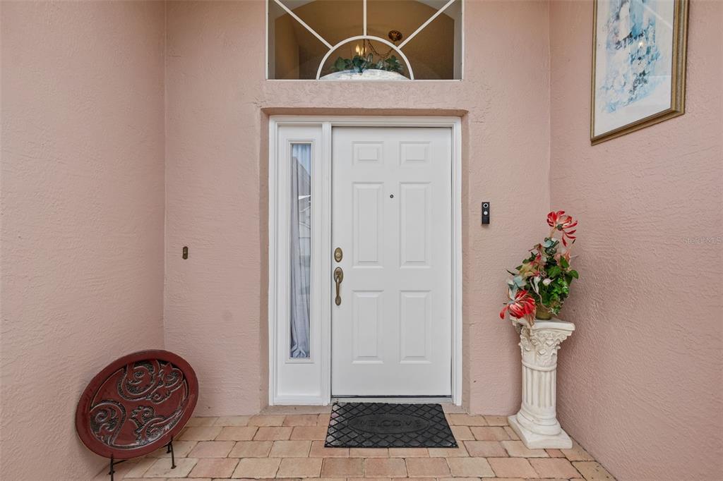 A white front door with a sidelight is framed by pink stucco walls and tile flooring — 1223 TIMBER TRACE DRIVE, WESLEY CHAPEL, FL