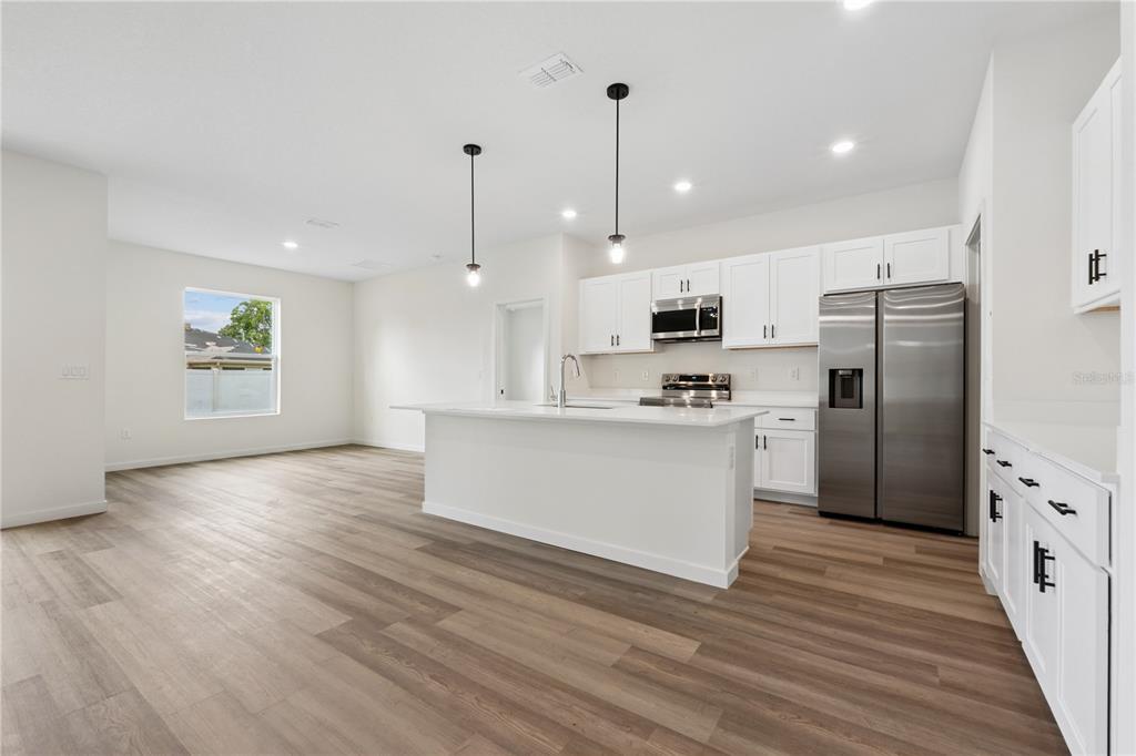 A modern kitchen features white cabinets, stainless steel appliances, a center island, and wood-look flooring — 67 PRESIDENT LANE, PALM COAST, FL