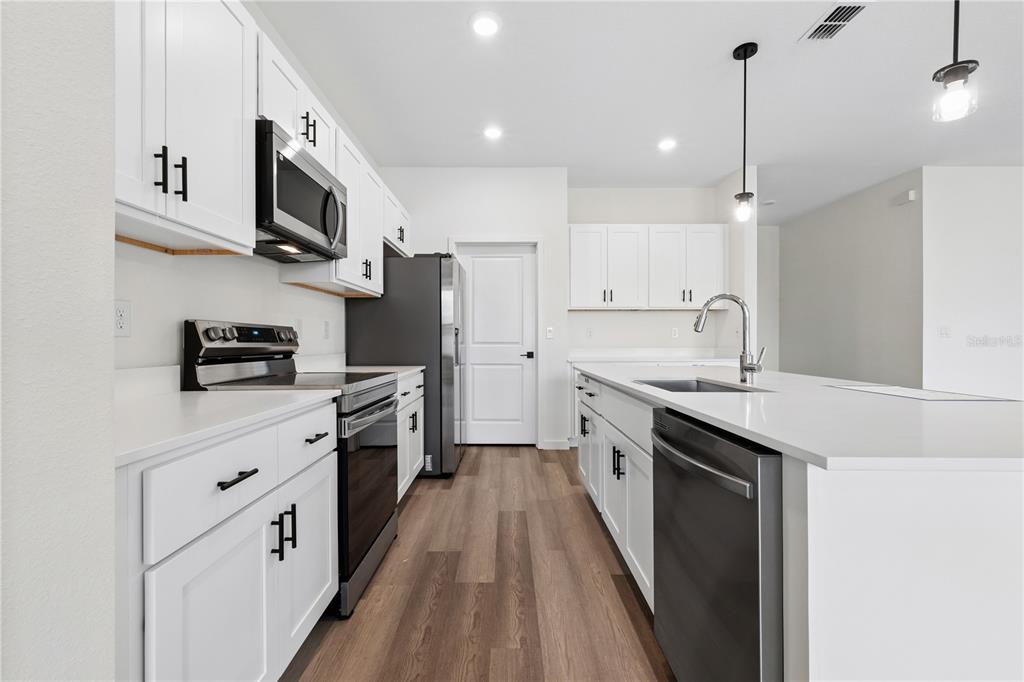 A modern kitchen features white cabinets, stainless steel appliances, a center island, and wood flooring — 67 PRESIDENT LANE, PALM COAST, FL