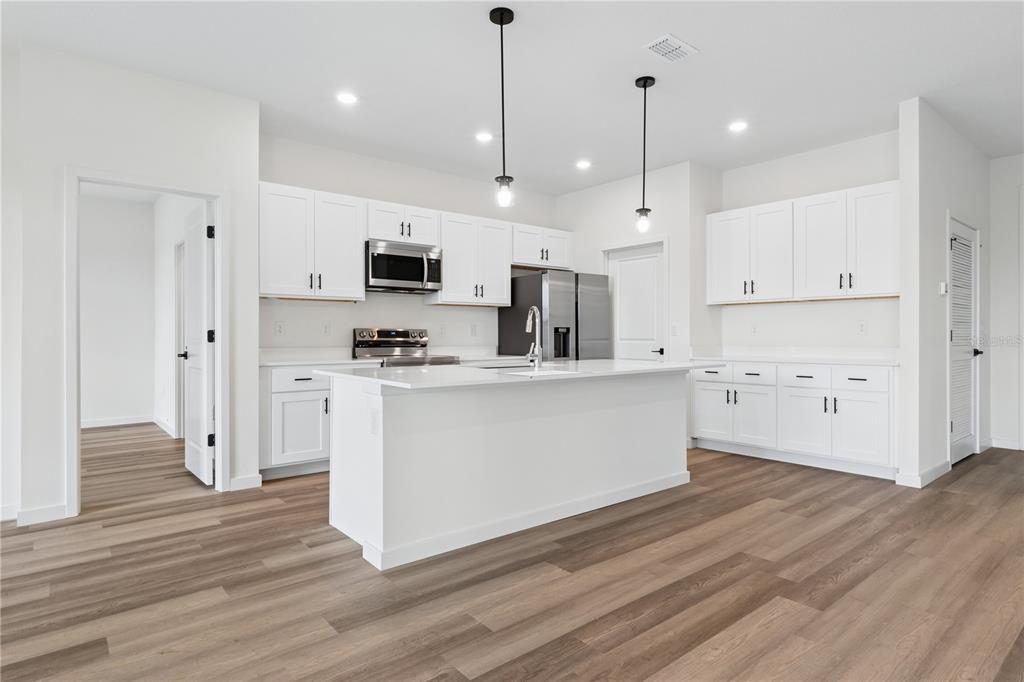 A modern kitchen features white cabinets, a central island, stainless steel appliances, and wood flooring — 67 PRESIDENT LANE, PALM COAST, FL