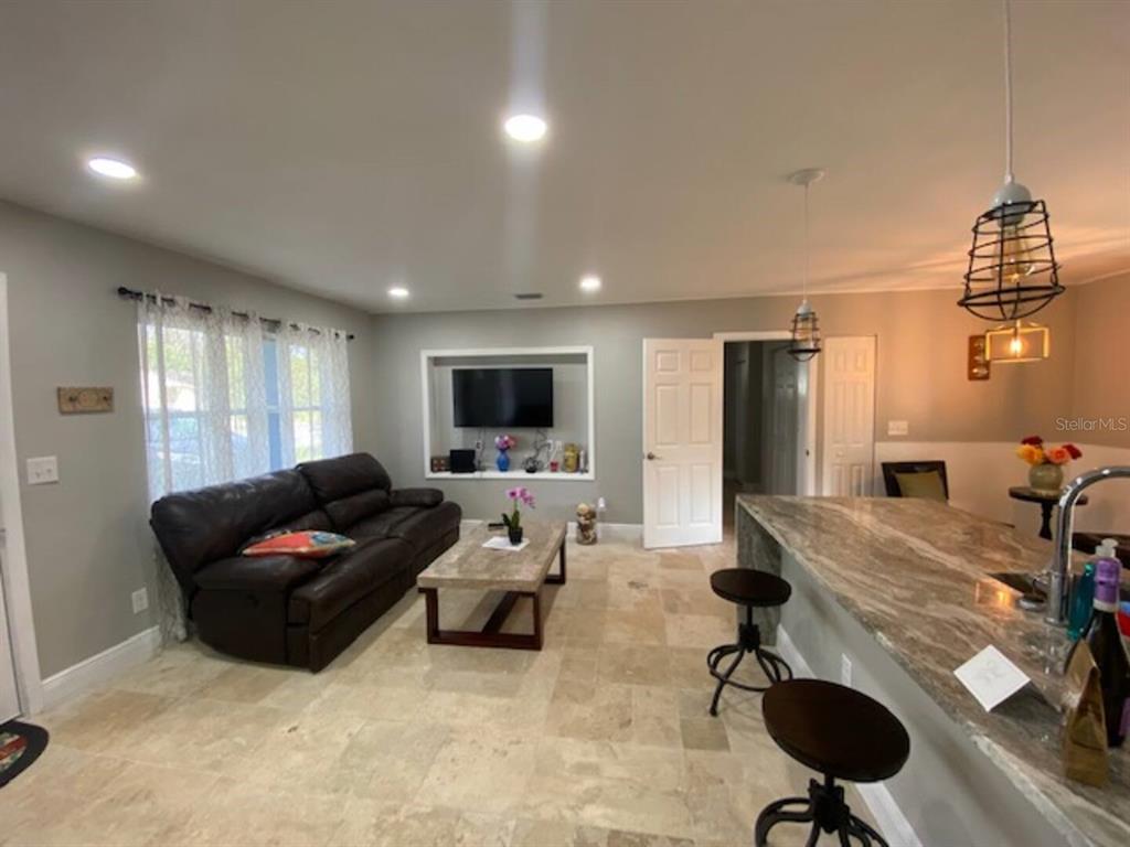 An open-concept living room and kitchen featuring tile flooring, a leather sofa, and stone countertops — 508 ULELAH AVENUE, PALM HARBOR, FL