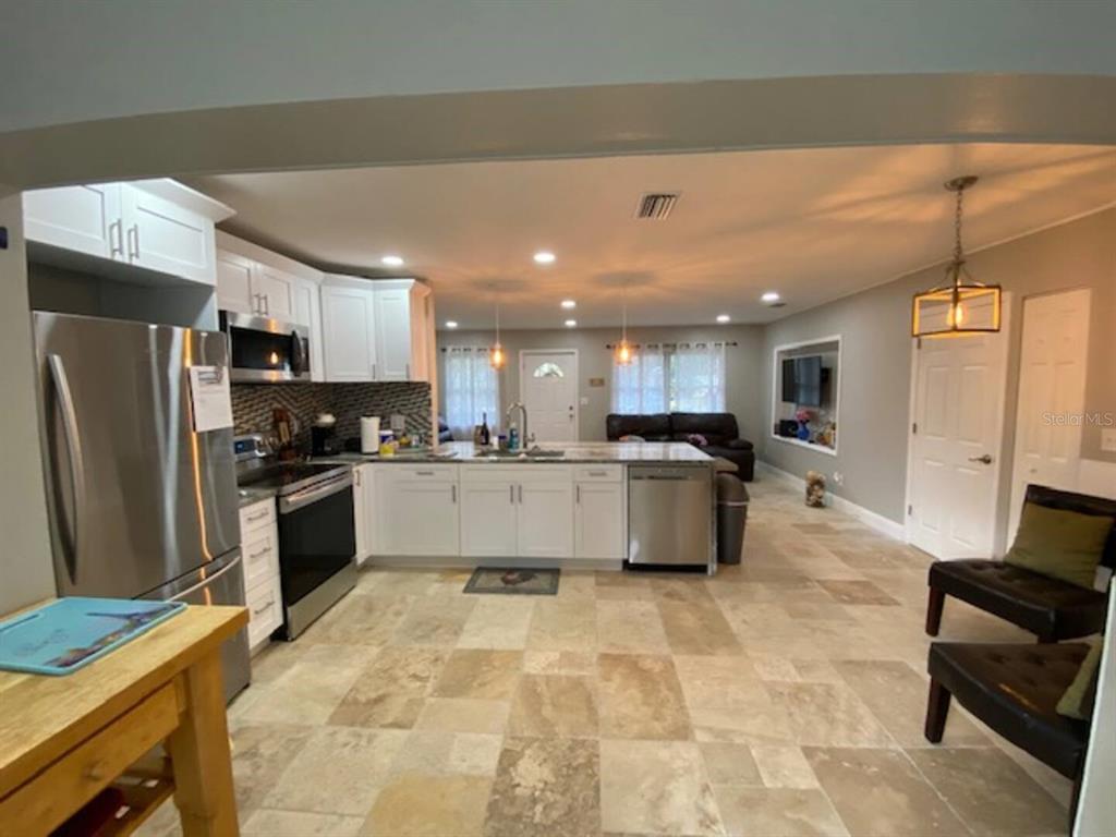 A kitchen with white cabinets, stainless steel appliances, and tile flooring opens to a living area — 508 ULELAH AVENUE, PALM HARBOR, FL