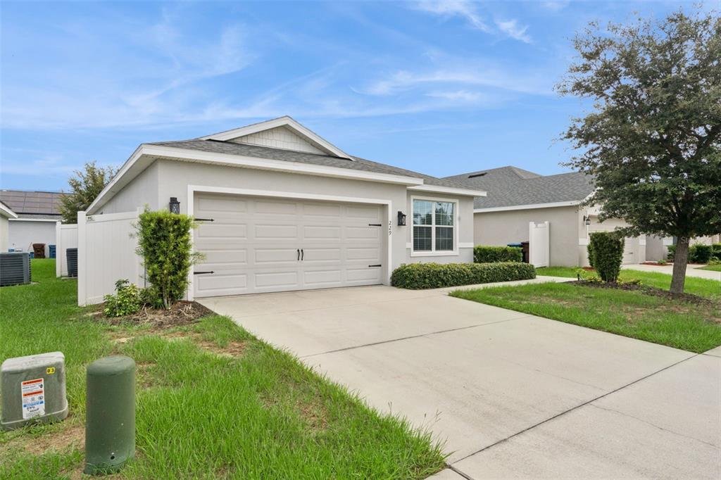 A single-story suburban house features a two-car garage, a concrete driveway, and a grassy lawn — 229 SANDESTIN DR, HAINES CITY, FL
