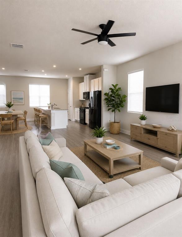 An open-concept living room and kitchen feature light wood flooring, neutral furniture, and a ceiling fan — 15084 CARAVAN AVENUE, ODESSA, FL
