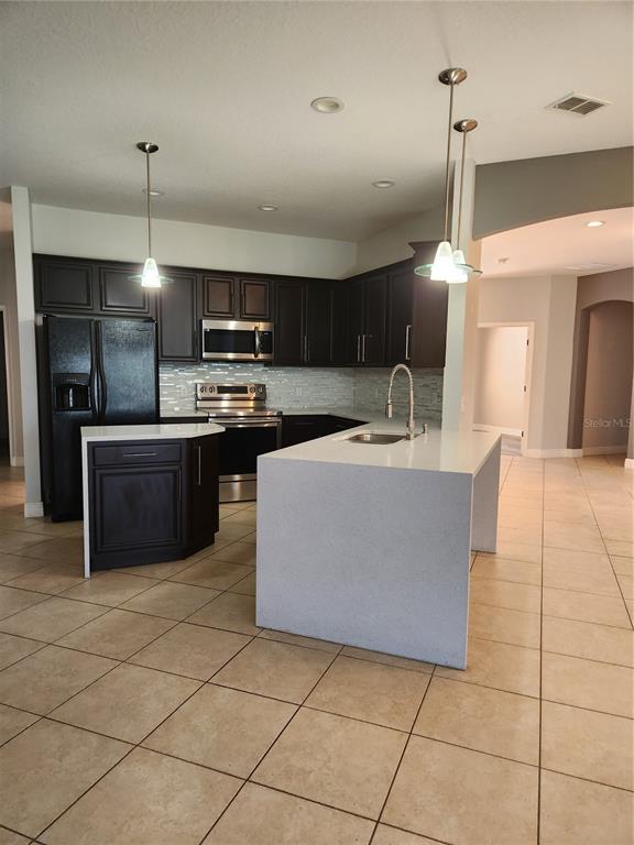 A kitchen features dark wood cabinetry, stainless steel appliances, and a large white island — 3507 SUNSET ISLES BLVD., KISSIMMEE, FL