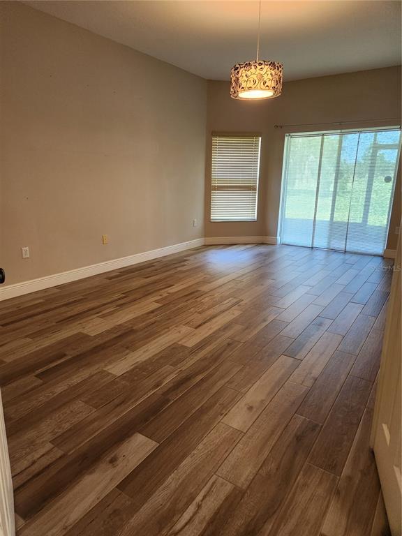 A living room with wood-look tile flooring, a hanging light fixture, and sliding glass doors — 3507 SUNSET ISLES BLVD., KISSIMMEE, FL