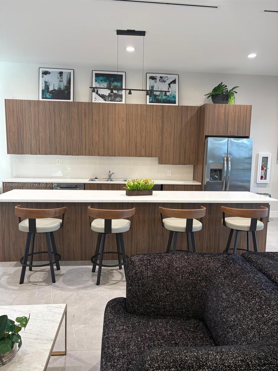 A modern kitchen features wood-grain cabinetry, a white countertop island, and four bar stools — 23320 SW 127th Ct, Homestead FL 33032, HOMESTEAD, FL