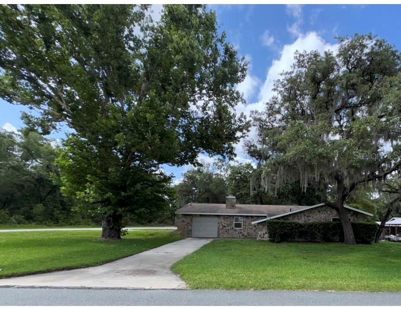 A single-story stone house with a concrete driveway and large trees in the front yard — 3000 E BRYANT STREET, INVERNESS, FL