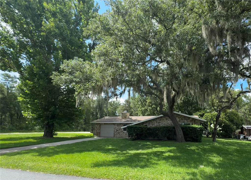 A stone-faced ranch house with a garage sits on a lawn under large trees — 3000 E BRYANT STREET, INVERNESS, FL