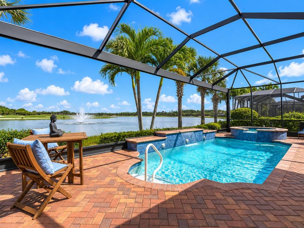 A screened-in patio features a brick-paved deck, a swimming pool, and a view of a lake — 10264 PORTO ROMANO DRIVE, MIROMAR LAKES, FL