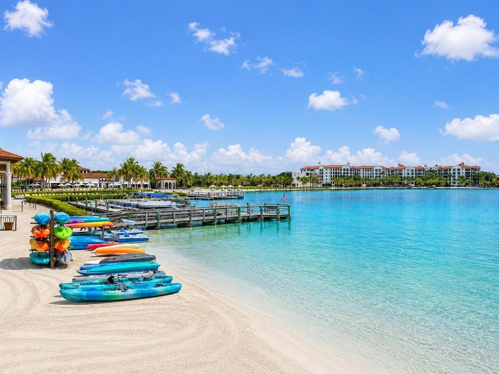 A sandy beach features a rack of colorful kayaks beside a wooden pier on turquoise water — 10264 PORTO ROMANO DRIVE, MIROMAR LAKES, FL