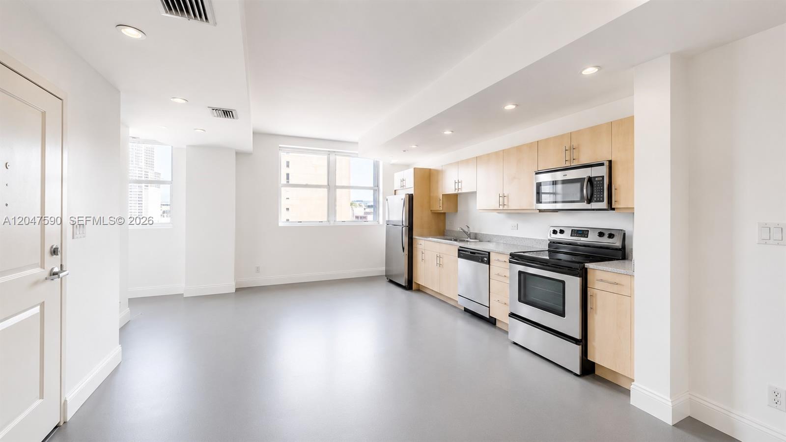 A kitchen with stainless steel appliances and light wood cabinets opens into a living area — 111 E Flagler St # 810, Miami FL 33131, MIAMI, FL