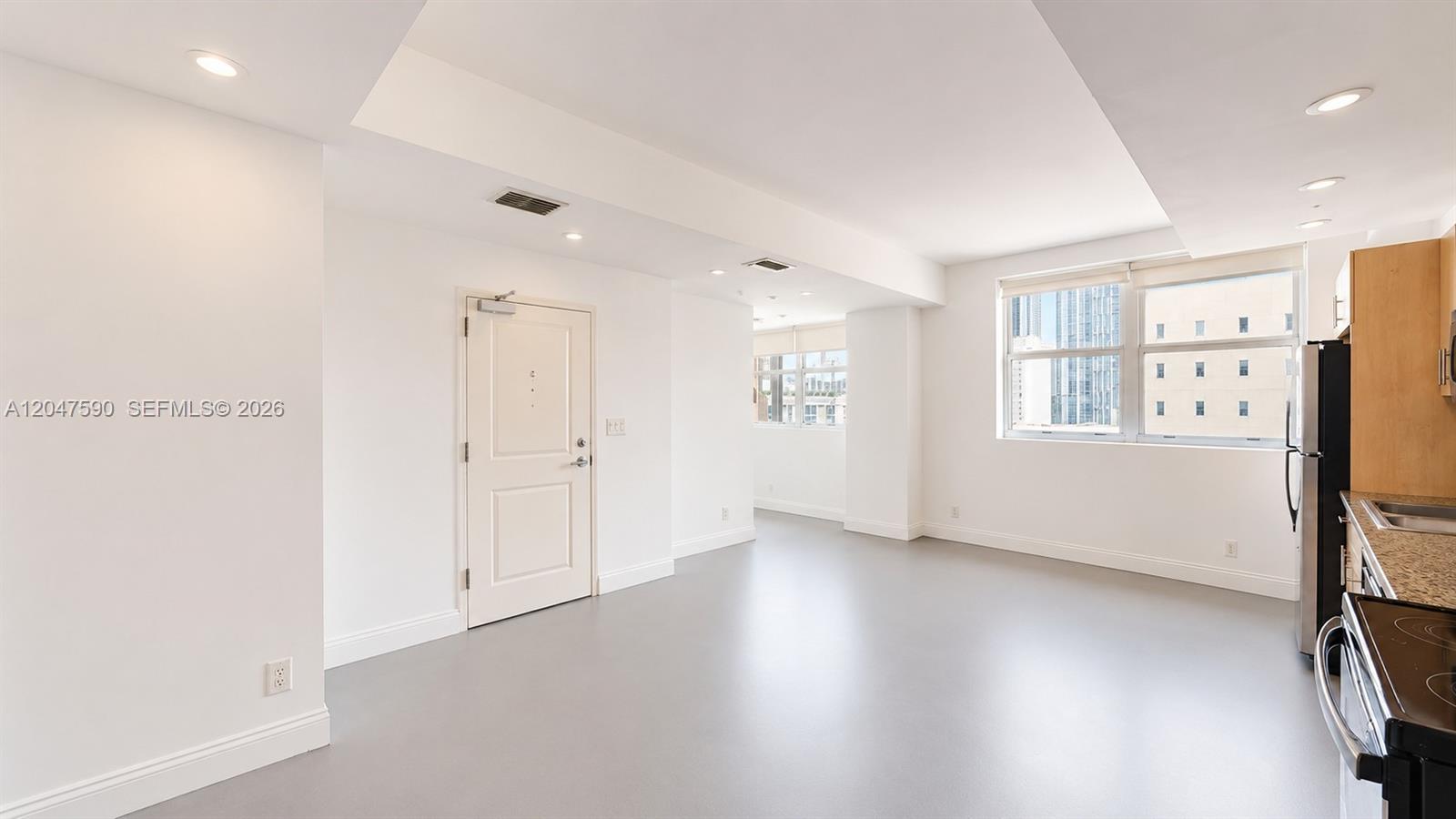This room features white walls, light gray flooring, a kitchen area, and large windows — 111 E Flagler St # 810, Miami FL 33131, MIAMI, FL