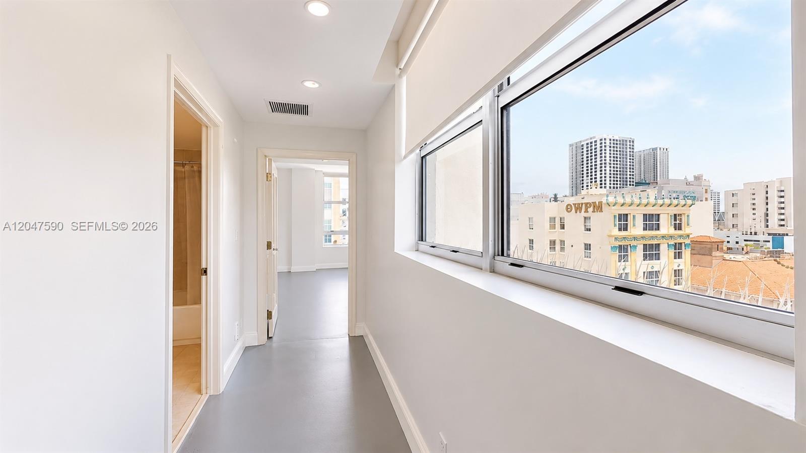 A hallway with gray flooring leads to a bathroom and a room with city views — 111 E Flagler St # 810, Miami FL 33131, MIAMI, FL