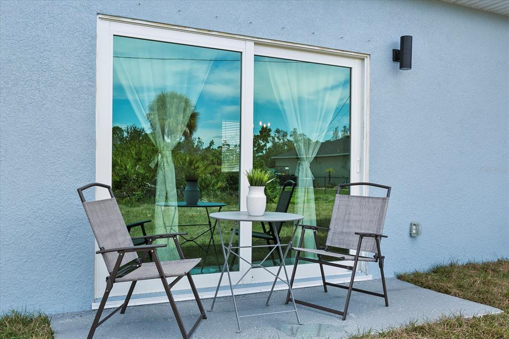 A small patio with a bistro set sits outside a blue house with sliding doors — 4306 JOSEPH STREET, PORT CHARLOTTE, FL