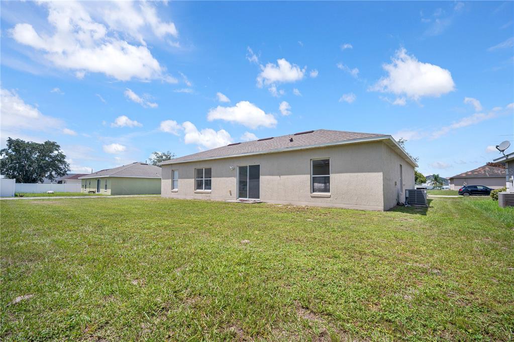 The rear exterior of a single-story house features a tan stucco finish and sliding glass doors — 433 LAKEVIEW ROAD, POINCIANA, FL