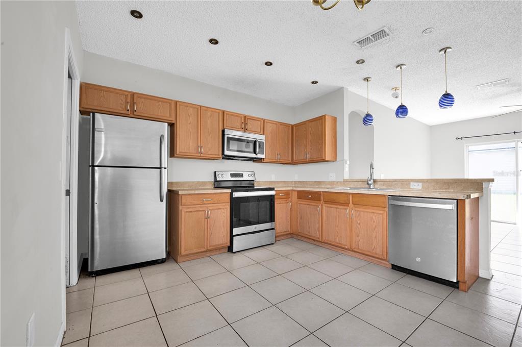 A kitchen features light wood cabinets, stainless steel appliances, and beige tile flooring — 433 LAKEVIEW ROAD, POINCIANA, FL