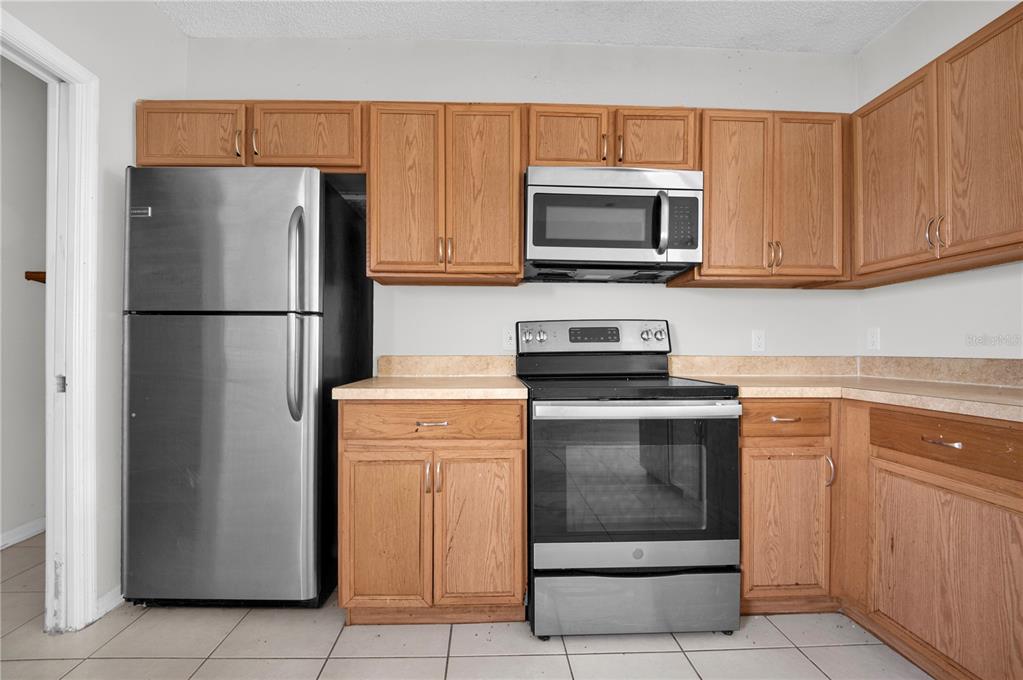 A kitchen features oak cabinets, stainless steel appliances, and light-colored countertops over tiled flooring — 433 LAKEVIEW ROAD, POINCIANA, FL