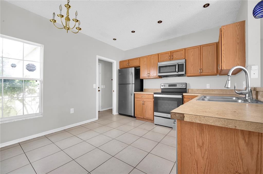 A kitchen features oak cabinets, stainless steel appliances, tile flooring, and a dining area chandelier — 433 LAKEVIEW ROAD, POINCIANA, FL