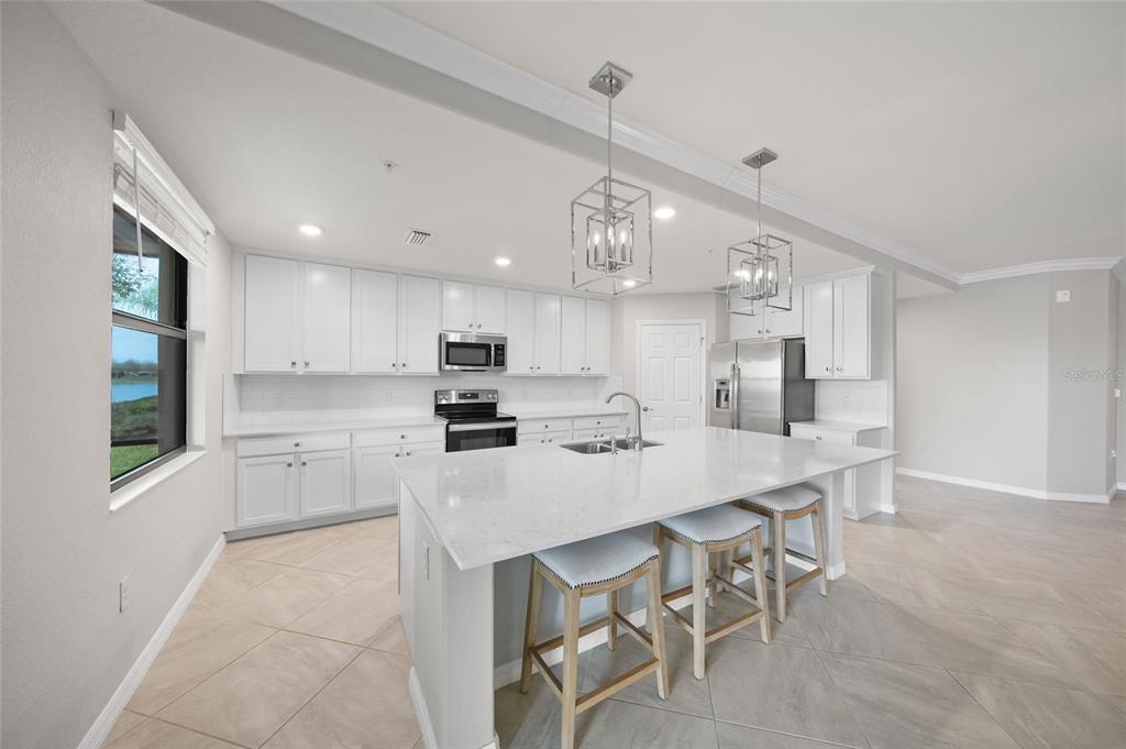 A modern kitchen features white cabinetry, a large quartz island, and stainless steel appliances — 10805 TARFLOWER DRIVE UNIT 102, VENICE, FL