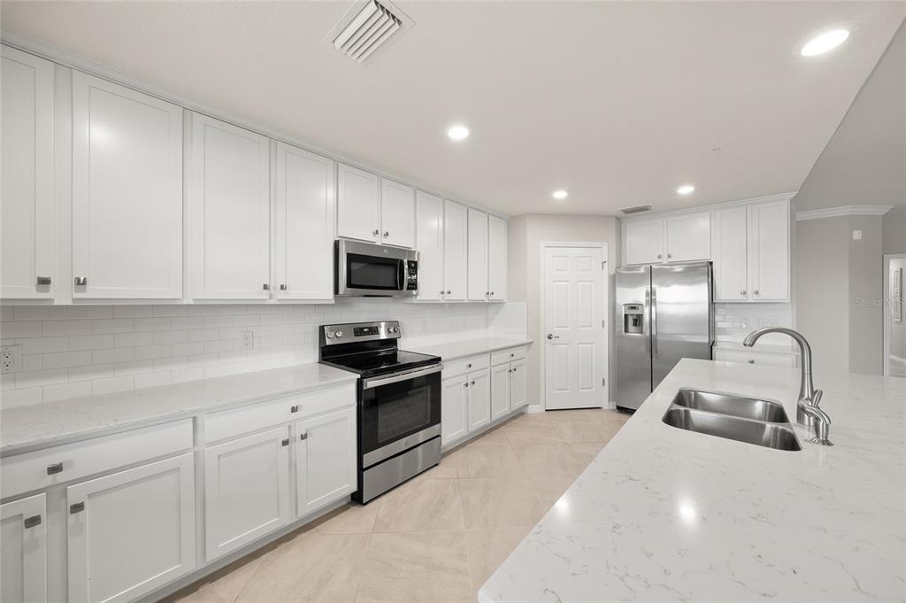 A bright kitchen features white cabinetry, stainless steel appliances, and a large quartz-topped island — 10805 TARFLOWER DRIVE UNIT 102, VENICE, FL