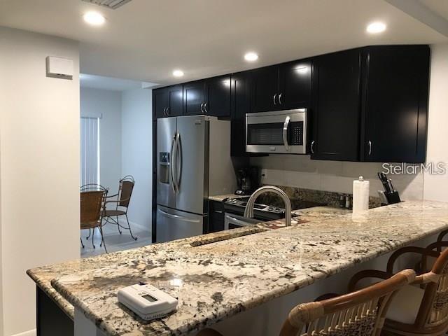 A kitchen features dark cabinets, granite countertops, stainless steel appliances, and a breakfast bar — 6892 W COUNTRY CLUB LANE, SARASOTA, FL