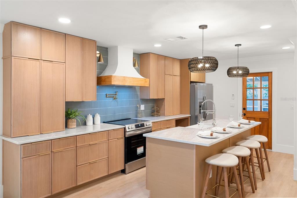 A modern kitchen features light wood cabinets, a blue tiled backsplash, and a central island — 6005 N ORANGE BLOSSOM AVENUE, TAMPA, FL
