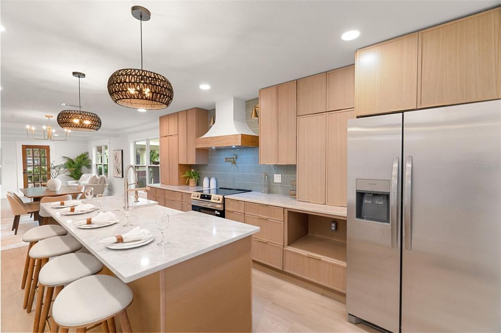 A modern kitchen features light wood cabinets, a marble-topped island, and stainless steel appliances — 6005 N ORANGE BLOSSOM AVENUE, TAMPA, FL