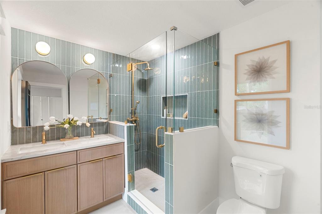 A bathroom features a wood vanity, blue vertical tile, a glass shower, and two framed prints — 6005 N ORANGE BLOSSOM AVENUE, TAMPA, FL