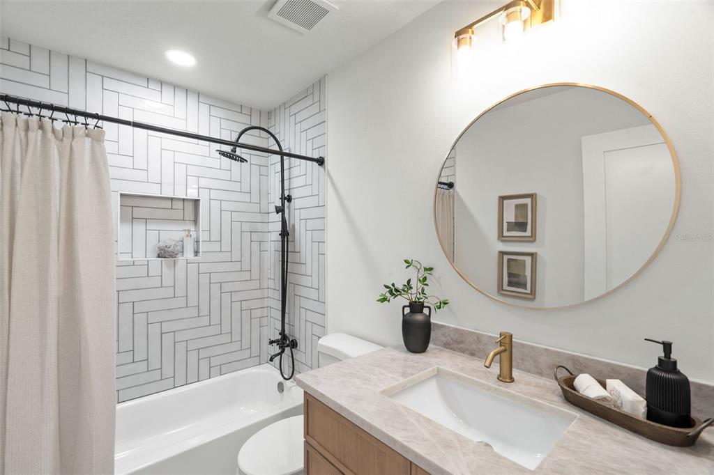 A bathroom features a herringbone-tiled shower, a round mirror, and a wood vanity with stone — 6005 N ORANGE BLOSSOM AVENUE, TAMPA, FL