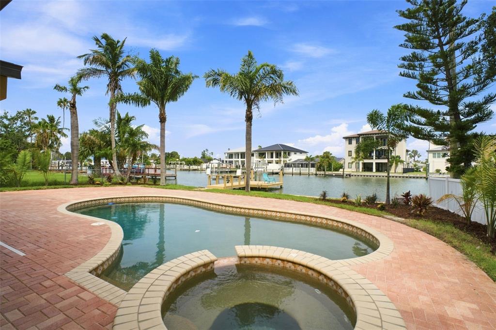 A backyard swimming pool and hot tub overlook a canal with docks and nearby houses — 15918 REDINGTON DRIVE, REDINGTON BEACH, FL