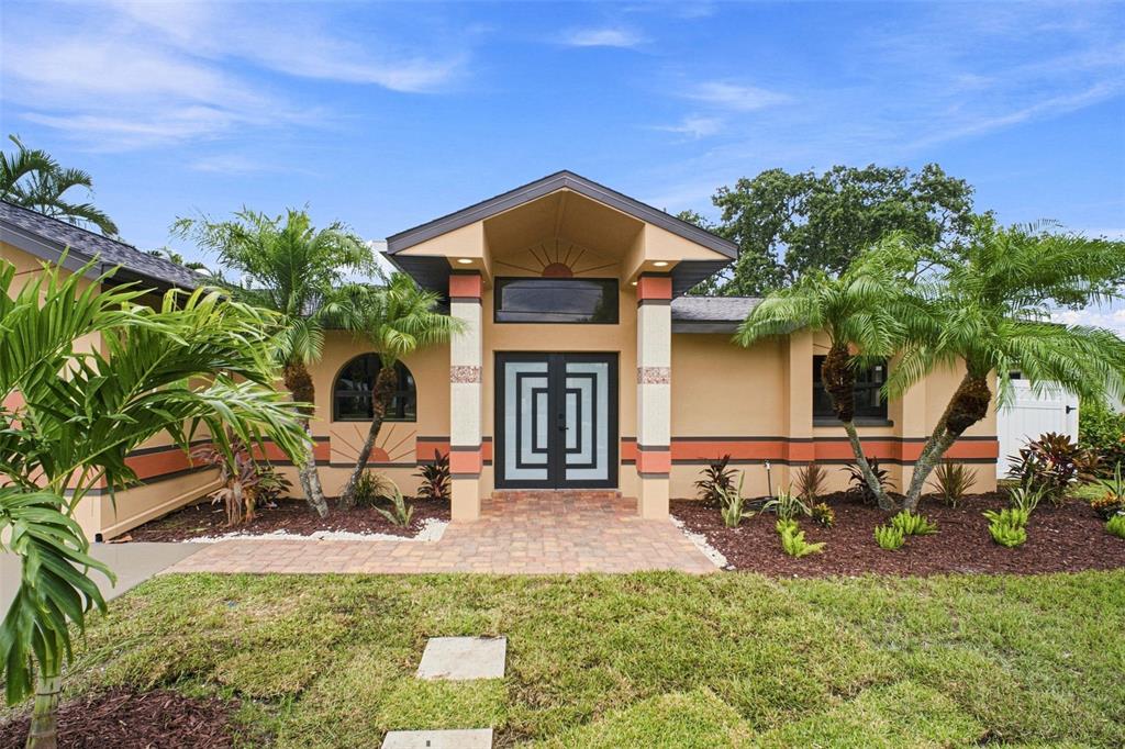 A single-story house with a tan exterior, double front doors, and palm trees in front — 15918 REDINGTON DRIVE, REDINGTON BEACH, FL