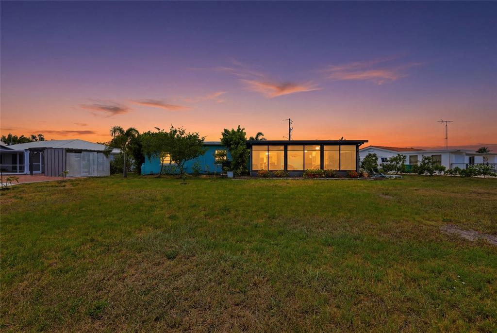 A blue house with a large glass-enclosed porch stands at sunset behind a grassy yard — 21444 HIGGS DRIVE, PORT CHARLOTTE, FL