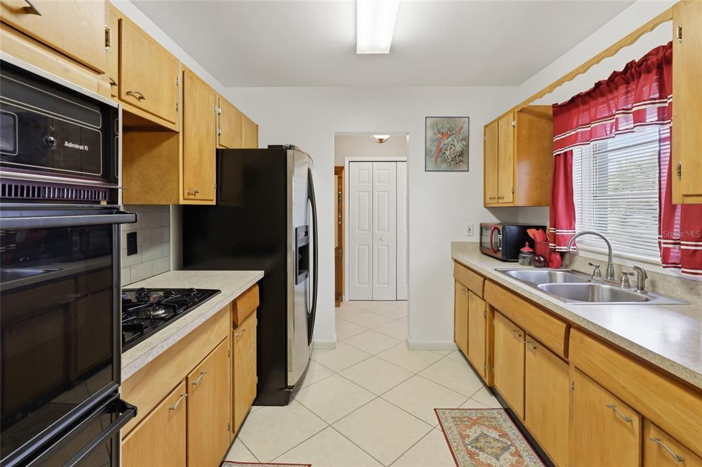 A galley kitchen features wood cabinets, stainless steel appliances, and a double basin sink — 21444 HIGGS DRIVE, PORT CHARLOTTE, FL