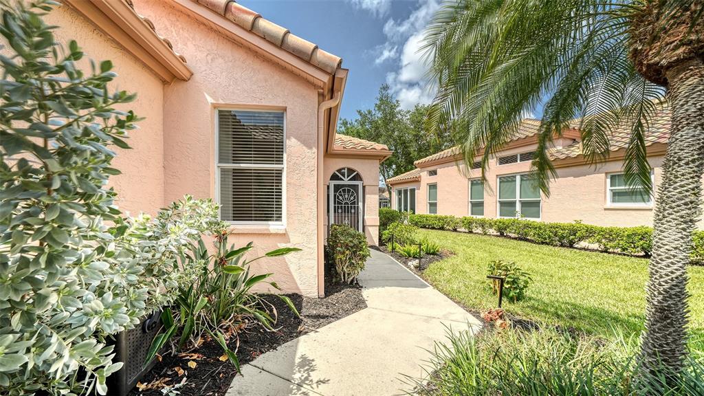 A concrete walkway leads to the entrance of a peach-colored house with a tile roof — 3799 MIRA LAGO DRIVE, SARASOTA, FL