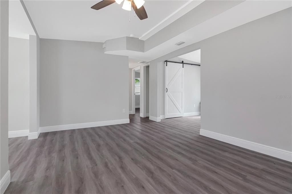 An empty room with gray walls, wood-look flooring, a ceiling fan, and a barn door — 2216 E 109TH AVENUE, TAMPA, FL